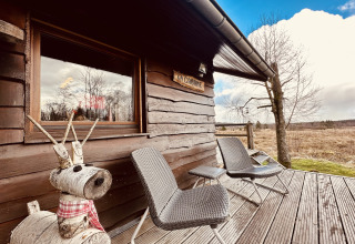 'La Cabane' chalet in België met twee stoelen, houten rendierbeeld en uitzicht op de natuur.