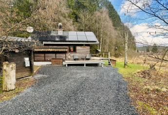 Billede af chalet 'La Cabane' i Belgien med solpaneler, terrasse og omgivet af skov og natur.
