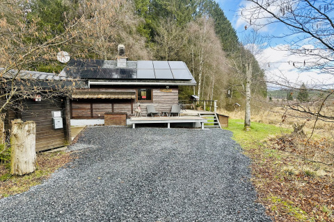 Foto van chalet 'La Cabane' in België met zonnepanelen, terras en omgeven door bosrijke natuur.