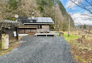 Foto van chalet 'La Cabane' in België met zonnepanelen, terras en omgeven door bosrijke natuur.