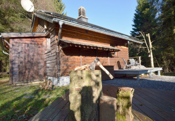 Træhytte kaldet La Cabane i Belgien med huggeblok, økse og terrasse omgivet af skov og natur.