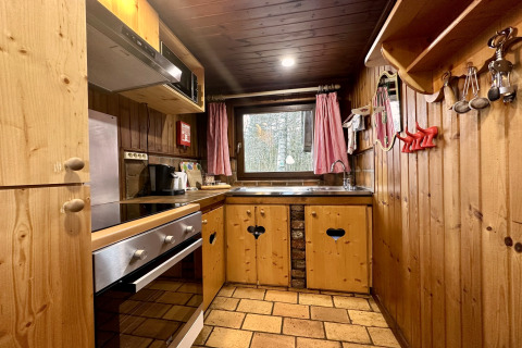 Cucina rustica in legno con forno, lavello e tende rosse nello chalet «La Cabane» in Belgio.