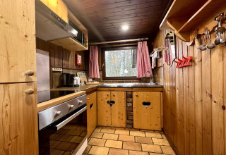Cucina rustica in legno con forno, lavello e tende rosse nello chalet «La Cabane» in Belgio.