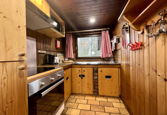 Træbeklædt køkken med ovn, vask og rødrutede gardiner i chalet 'La Cabane' i Belgien.