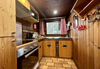 Gezellige houten keuken met oven, gootsteen en rood geruite gordijnen in chalet 'La Cabane', België.