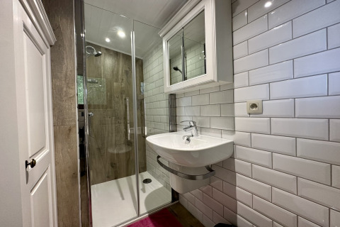 Moderne badkamer in chalet La Cabane in België met glazen douche, wastafel en witte wandtegels.