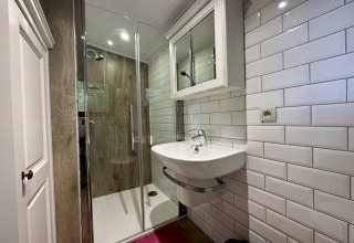 Moderne badkamer in chalet La Cabane in België met glazen douche, wastafel en witte wandtegels.