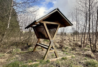Træfoderstativer med tag i et naturligt landskab ved La Cabane, en chalet i Belgien.