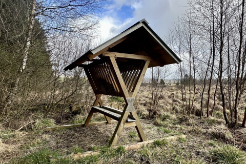 Houten voederrek met dak in een natuurlijk landschap bij La Cabane, chalet in België.