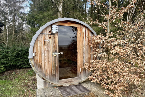 Houten saunaton bij chalet La Cabane in België, buiten geplaatst en omgeven door groene en droge bomen.