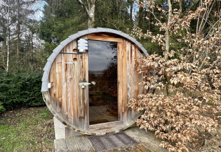 Houten saunaton bij chalet La Cabane in België, buiten geplaatst en omgeven door groene en droge bomen.