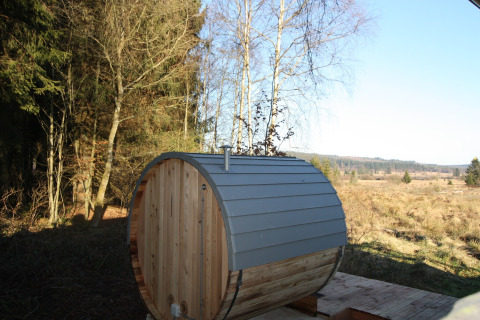 Buitensauna in vatvorm bij chalet La Cabane in België, omgeven door bos en open velden onder een heldere hemel.