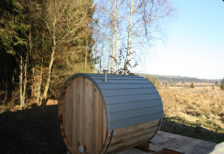 Buitensauna in vatvorm bij chalet La Cabane in België, omgeven door bos en open velden onder een heldere hemel.