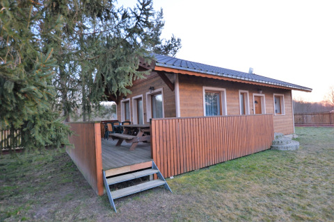 Chalet in legno Marcela con veranda coperta, panchine e giardino recintato tra gli alberi.