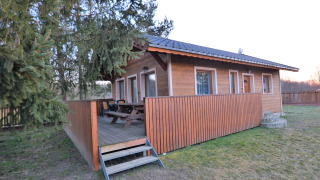 Houten chalet Marcela met overdekt terras, picknicktafels en omheinde tuin met bomen en gras.