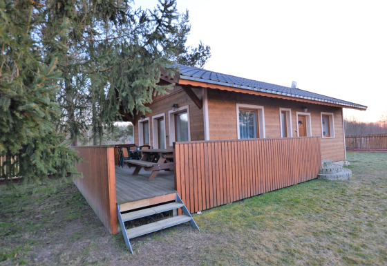 Chalet in legno Marcela con veranda coperta, panchine e giardino recintato tra gli alberi.