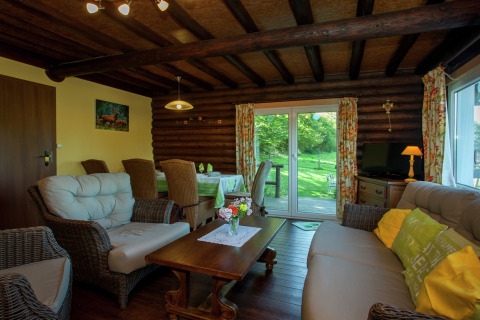 Wohnzimmer im Chalet Les Muguets in Belgien mit Holzwänden, Korbmöbeln und Blick auf den Garten.