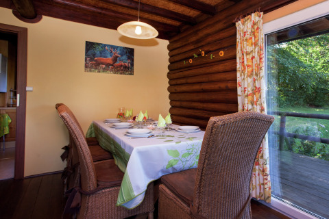 Esszimmer im Chalet 'Les Muguets' in Belgien mit gedecktem Tisch, Holzwänden und Gartenausblick.