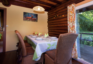 Esszimmer im Chalet 'Les Muguets' in Belgien mit gedecktem Tisch, Holzwänden und Gartenausblick.