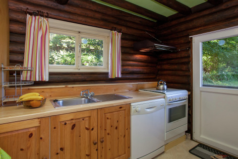 Gemütliche Holzküche im Chalet Les Muguets in Belgien mit Fenster, Herd, Spüle und Geschirrspüler.