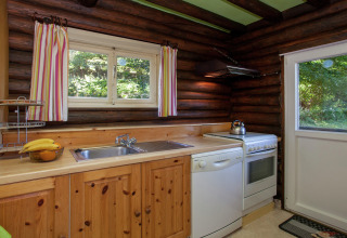 Gemütliche Holzküche im Chalet Les Muguets in Belgien mit Fenster, Herd, Spüle und Geschirrspüler.