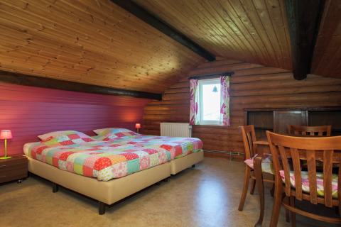 Gemütliches Schlafzimmer im Chalet Les Muguets, Belgien, mit Holzdecke, Doppelbett und Essbereich.