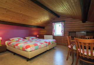 Gemütliches Schlafzimmer im Chalet Les Muguets, Belgien, mit Holzdecke, Doppelbett und Essbereich.