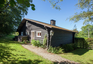 Gemütliches Blockhaus-Chalet Les Muguets in Belgien, umgeben von grüner Wiese und Bäumen bei Sonnenschein.