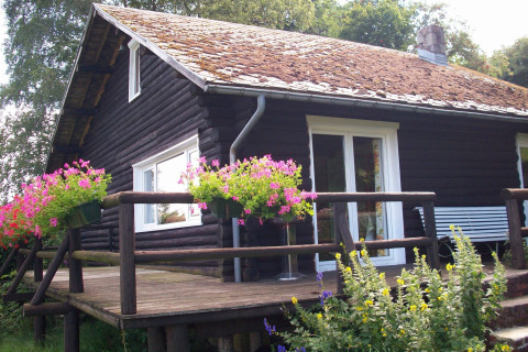 Gemütliches Chalet namens Les Muguets in Belgien mit blühenden Blumen auf der Holzveranda und Natur.
