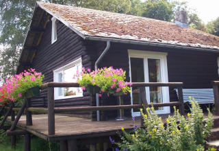 Gemütliches Chalet namens Les Muguets in Belgien mit blühenden Blumen auf der Holzveranda und Natur.