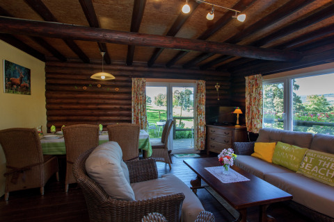 Gemütliches Wohnzimmer im Chalet «Les Muguets» in Belgien mit Holzwänden, Korbmöbeln und Gartenblick.