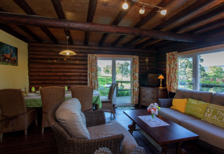 Gemütliches Wohnzimmer im Chalet «Les Muguets» in Belgien mit Holzwänden, Korbmöbeln und Gartenblick.