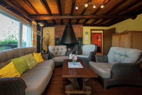 Gemütliches Chalet 'Les Muguets' in Belgien mit Holzbalkendecke, Kamin, Rattanmöbeln und Sofas.