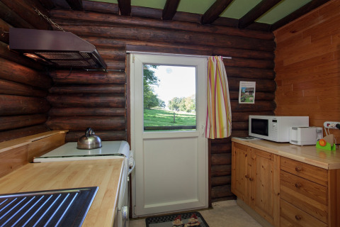 Holzküche im Chalet Les Muguets, Belgien, mit Blick nach draußen auf grüne Wiesen durch die Tür.