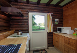 Holzküche im Chalet Les Muguets, Belgien, mit Blick nach draußen auf grüne Wiesen durch die Tür.