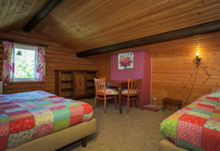 Gemütliches Schlafzimmer im Chalet Les Muguets, Belgien, mit Holzdecke, zwei Betten und bunter Einrichtung.