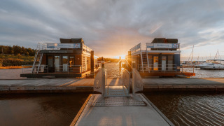 Houseboat at Bärwalder See during sunset, moored at a peaceful dock with boats and calm water views.