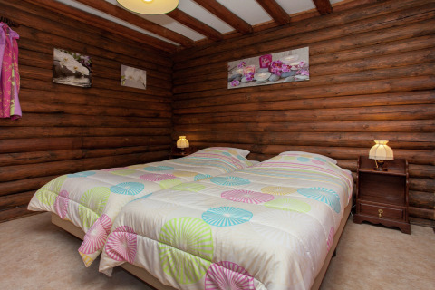 Schlafzimmer im Chalet Les Muguets in Belgien mit Holzwänden, Doppelbett und bunter Bettwäsche.