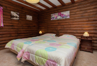 Schlafzimmer im Chalet Les Muguets in Belgien mit Holzwänden, Doppelbett und bunter Bettwäsche.