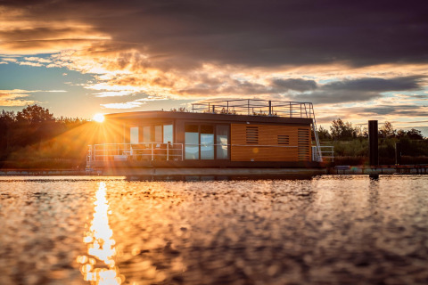 Sunset view of Houseboat am Bärwalder See with modern houseboat reflecting on calm lake water.