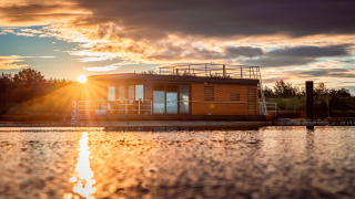 Solnedgang over Houseboat am Bärwalder See med en moderne husbåd på søens rolige overflade.