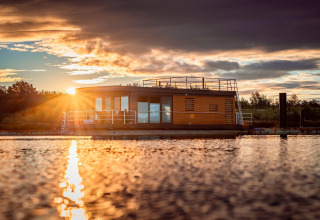 Tramonto sulla Houseboat am Bärwalder See, casa galleggiante moderna riflessa sull’acqua calma.