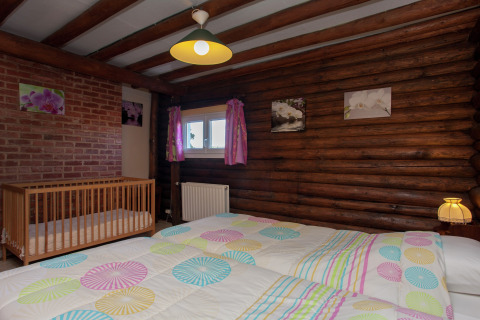 Schlafzimmer im Chalet 'Les Muguets' in Belgien mit Holzwänden, Babybett, buntem Bett und Dekor.