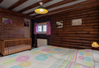 Schlafzimmer im Chalet 'Les Muguets' in Belgien mit Holzwänden, Babybett, buntem Bett und Dekor.