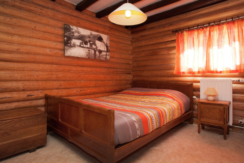 Schlafzimmer im Chalet 'Les Muguets' in Belgien mit Holzwänden, orange Gardinen und Doppelbett.