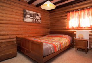Schlafzimmer im Chalet 'Les Muguets' in Belgien mit Holzwänden, orange Gardinen und Doppelbett.