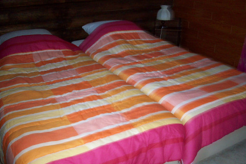 Zwei Einzelbetten mit bunten gestreiften Decken in einem Chalet «Les Muguets» in Belgien, gemütliches Ambiente.