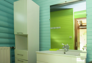 Badezimmer mit mintgrünen Wänden, Spiegel, weißem Schrank und Waschbecken im Chalet „Les Muguets“ in Belgien.