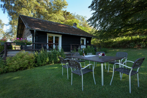 Chalet 'Les Muguets' in Belgien mit Gartentisch, sechs Stühlen und üppigem Grün im Freien vor dem Haus.