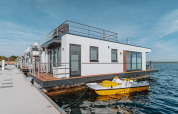 Moderne woonboot aan de Gräbendorfer See met dakterras en gele waterfiets op een zonnige dag.